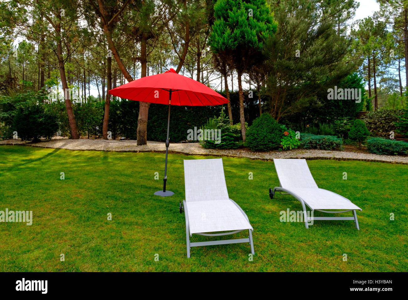 Zwei weiße Stoff-Lounge-Sesseln und einem roten Sonnenschirm auf einer Wiese im Garten Stockfoto