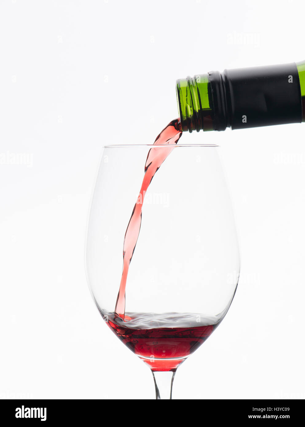 Rotwein aus der Flasche im Weinglas gießen. Isoliert auf weißem Hintergrund. Stockfoto