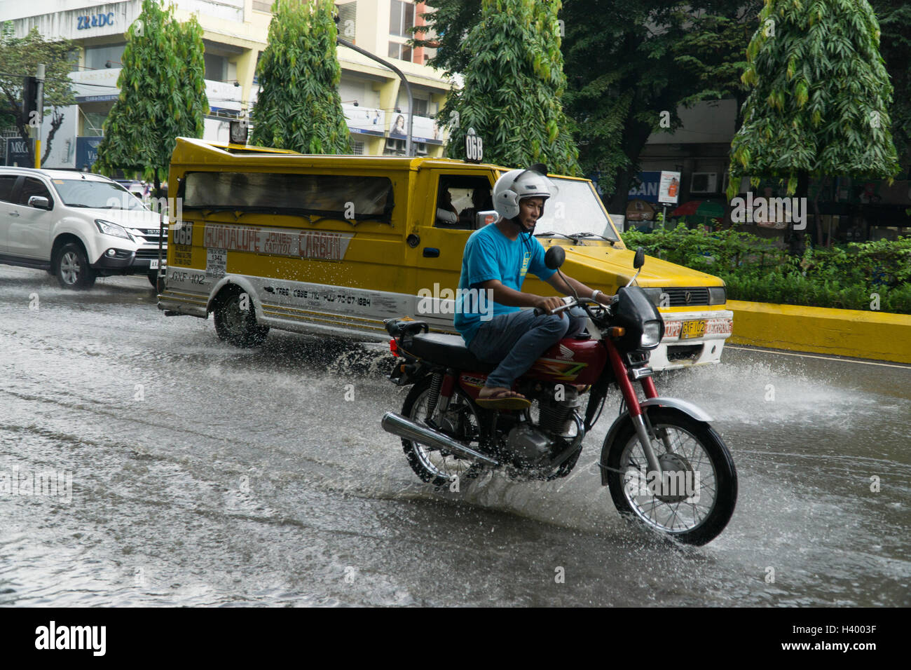 Ein Mann fährt ein Motorrad durch einen überfluteten Teil der Straße in Cebu City, Philippinen Stockfoto
