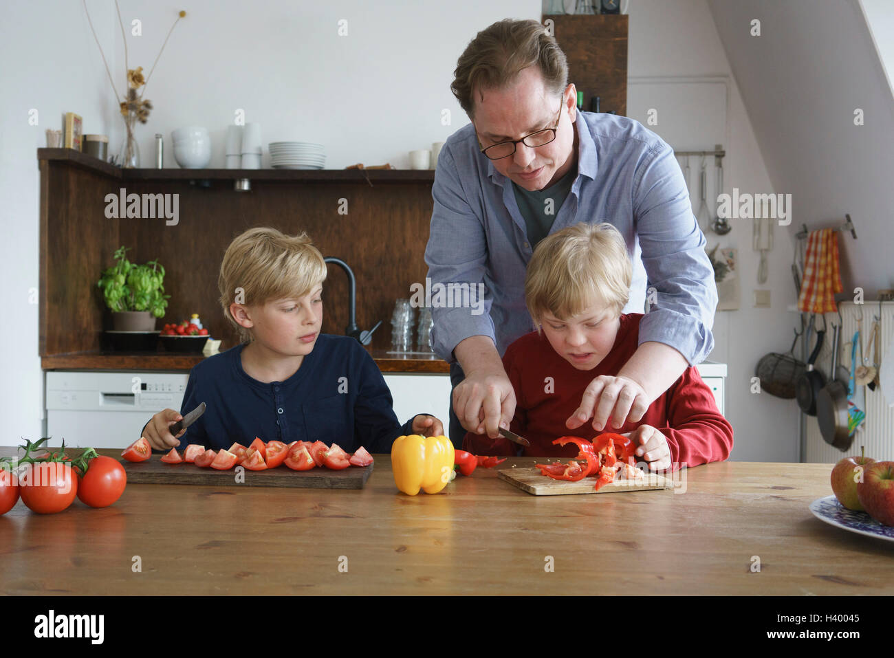 Vater Unterstützung deaktiviert Sohn um Gemüse Hacken mit jungen am Tisch in der Küche Stockfoto