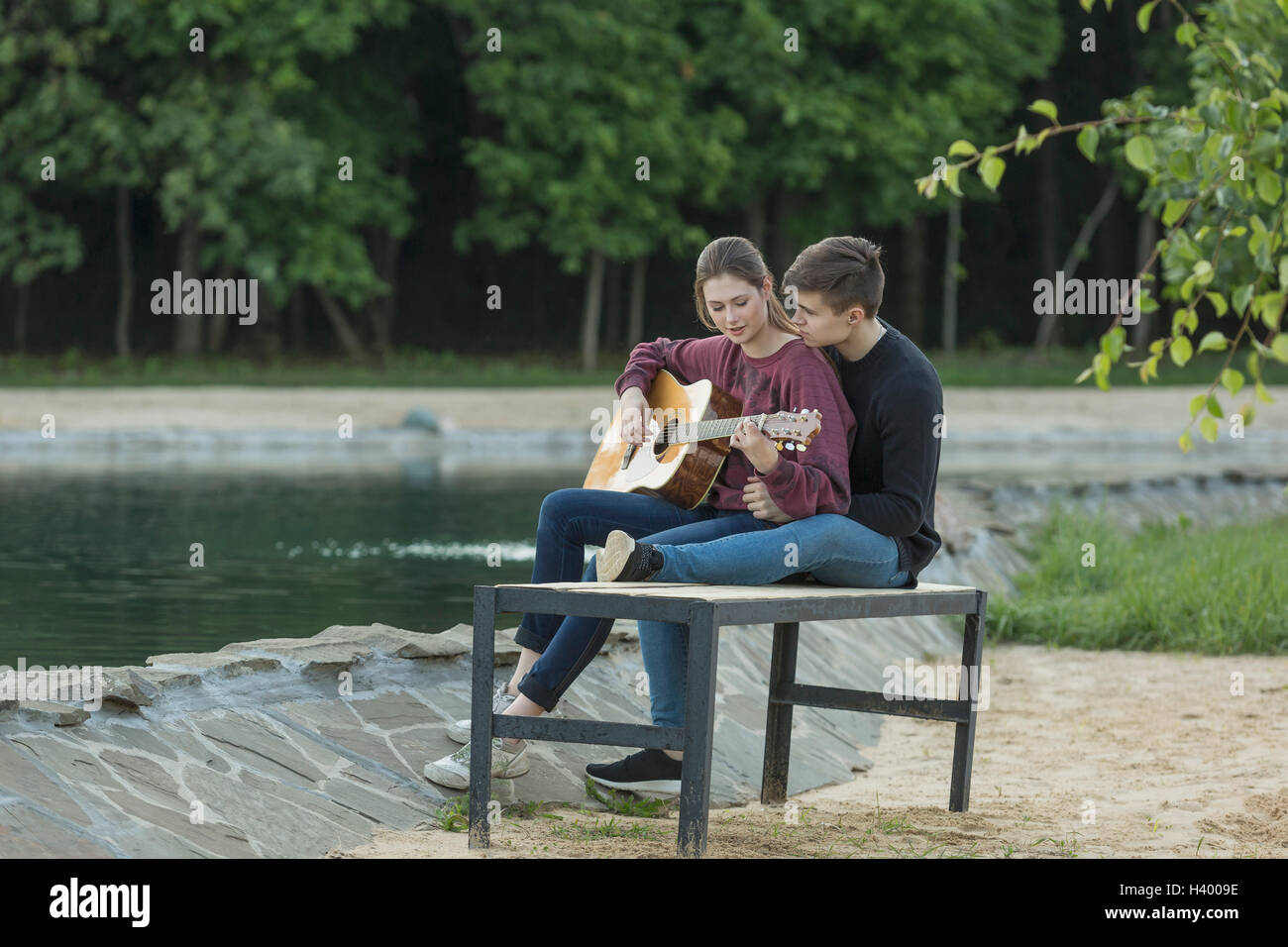 Liebevollen Mann mit Freundin Gitarre spielen auf Parkbank See ruht Stockfoto