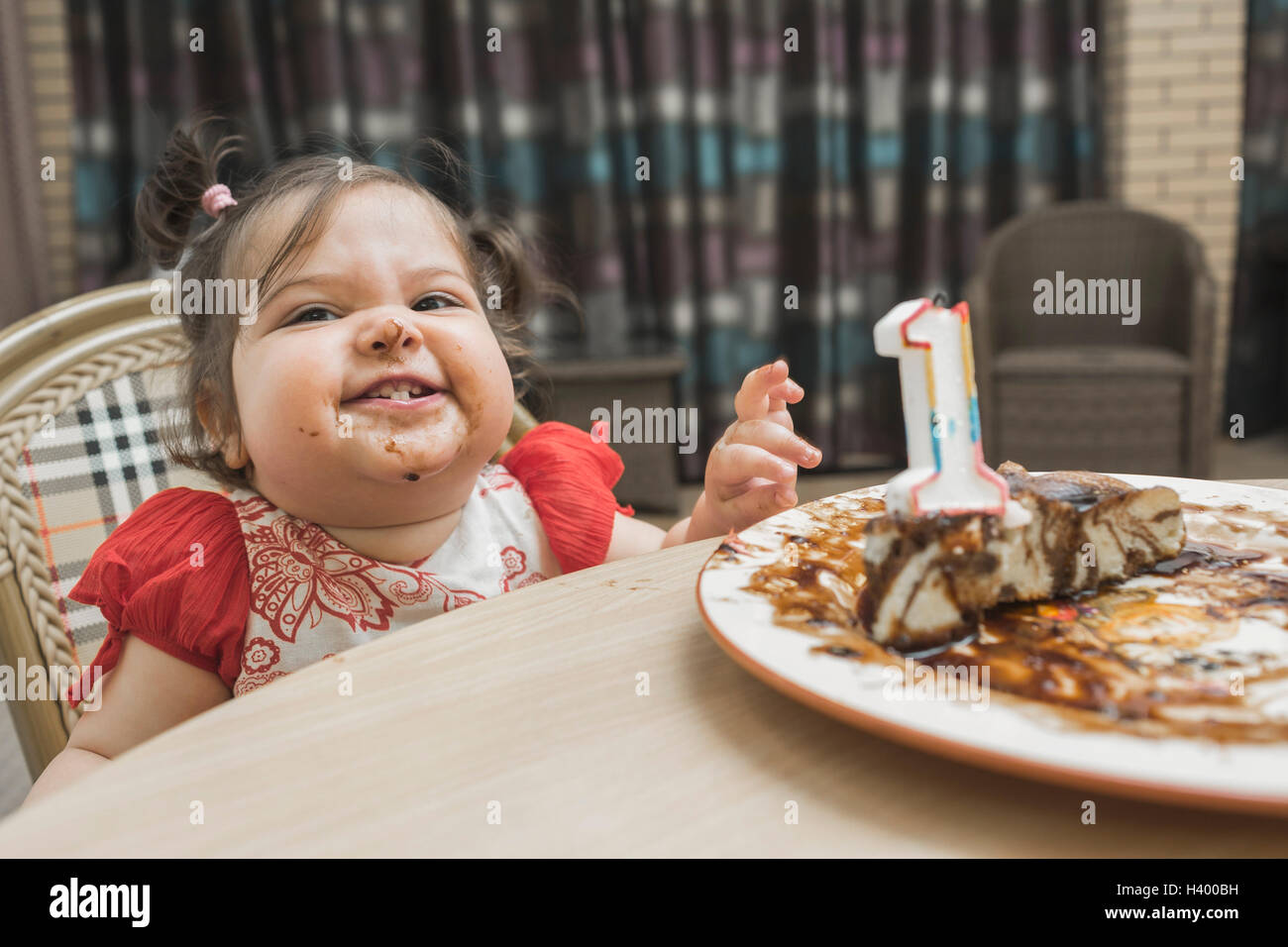 Nettes Mädchen mit chaotisch Gesicht mit Geburtstagskuchen am Tisch Stockfoto