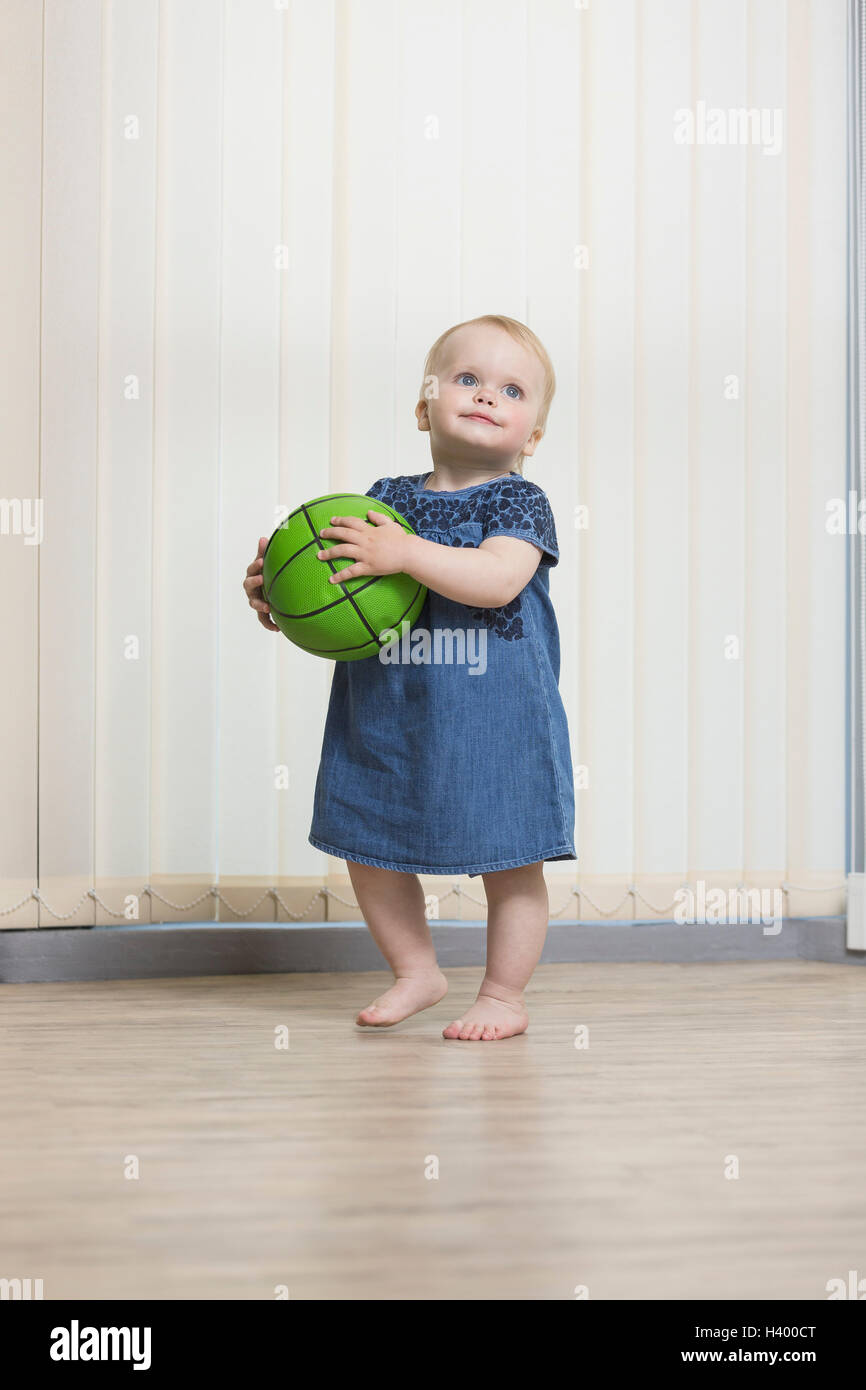 Niedliche Mädchen spielen mit Ball stehend gegen Vorhänge zu Hause Stockfoto