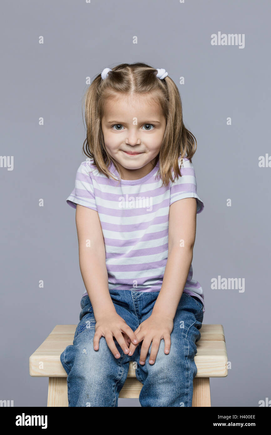 Porträt der lächelnde Mädchen sitzen auf hölzernen Schemel vor grauem Hintergrund Stockfoto