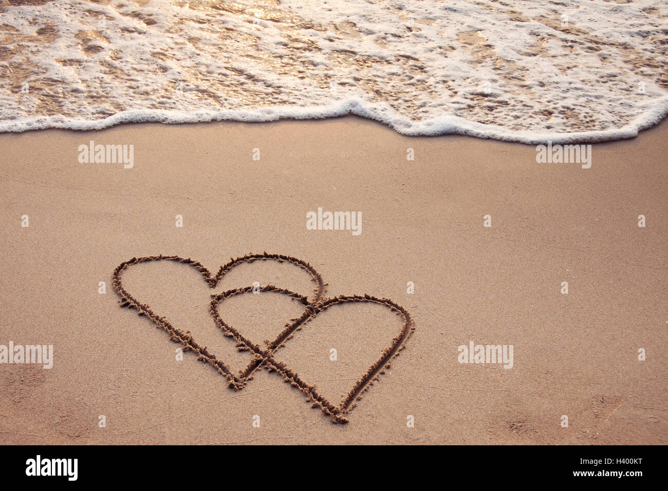 Herzen in den Sand mit Seafoam und Welle gezeichnet Stockfoto