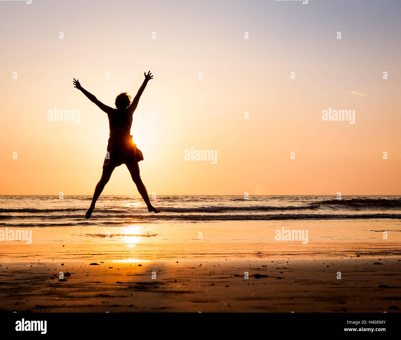 Glückliche Frau sprang Hände am Strand bei Sonnenuntergang mit Meer Hintergrund Stockfoto
