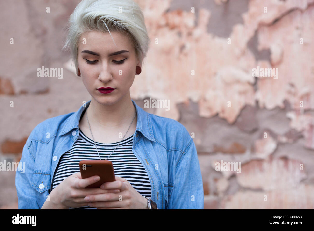 Schöne Frau mit Telefon stehend gegen alte Wand Stockfoto