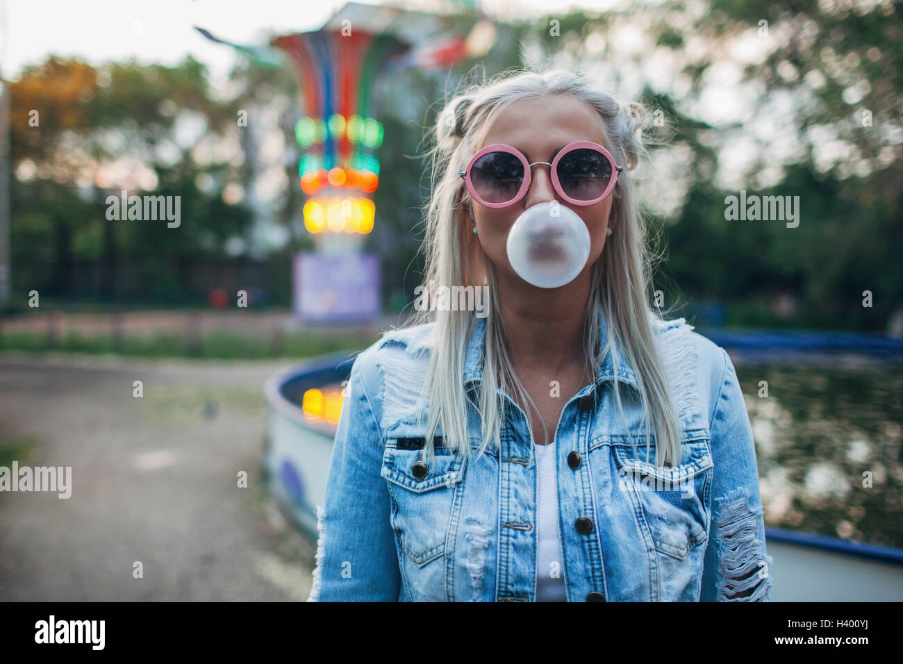 Porträt der jungen Frau mit Sonnenbrille während bläst Kaugummi im Freizeitpark Stockfoto