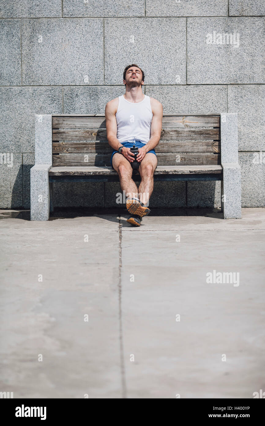 Müde junger Mann sitzt auf Holzbank an Wand Stockfoto