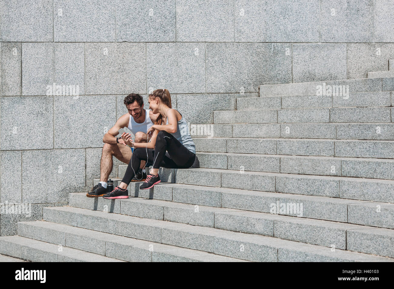 Glückliche Frau zeigt Smartphone Freund sitzend auf Schritte durch die Wand Stockfoto