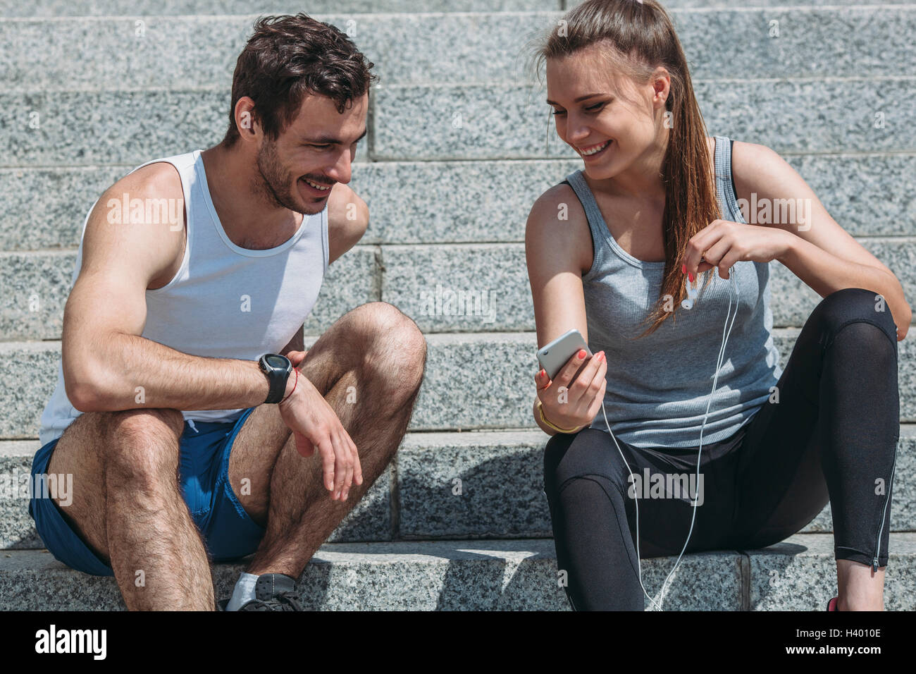 Stets gut gelaunte Frau zeigt Smartphone an männlichen Freund sitzend auf Schritte Stockfoto