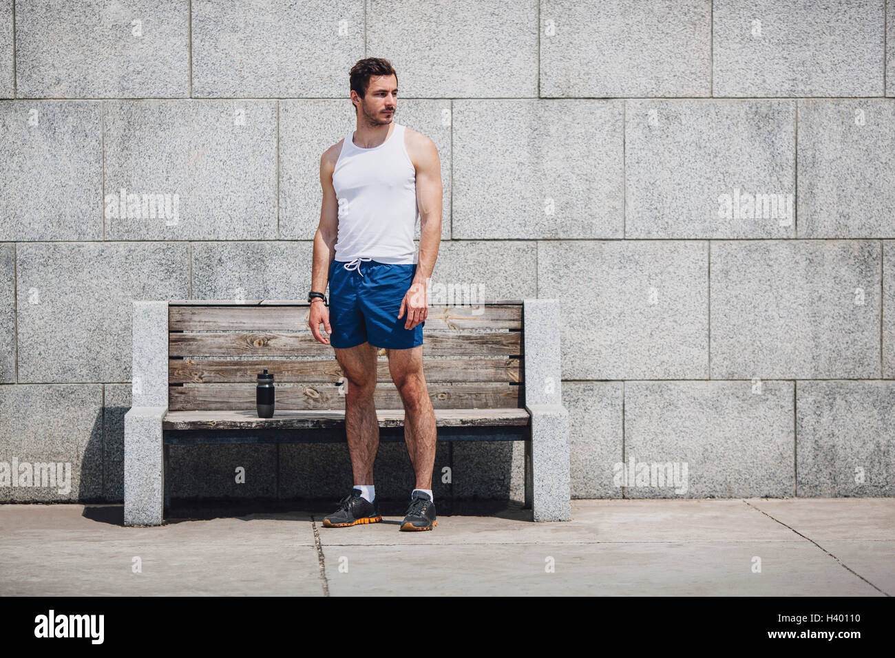 Ernsthafte Sportler von Holzbank auf Bürgersteig Wand stehend Stockfoto