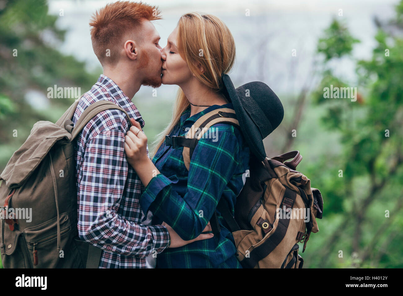 Liebespaar tragen Rucksäcke küssen im stehen am Wald Stockfoto