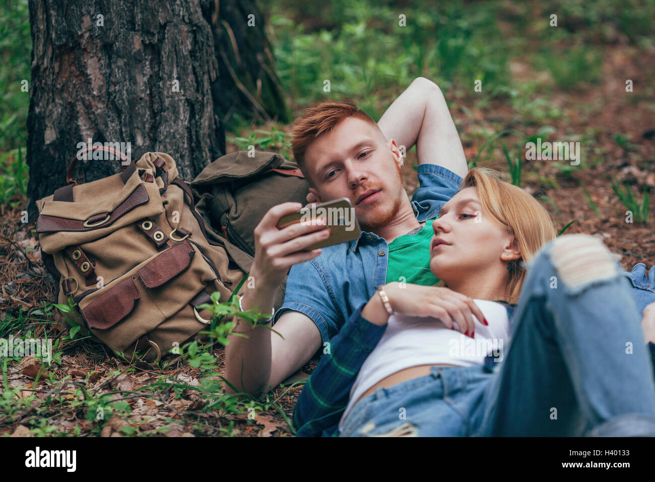 Junges Paar sucht in Smartphone liegend vom Baum im Wald Stockfoto