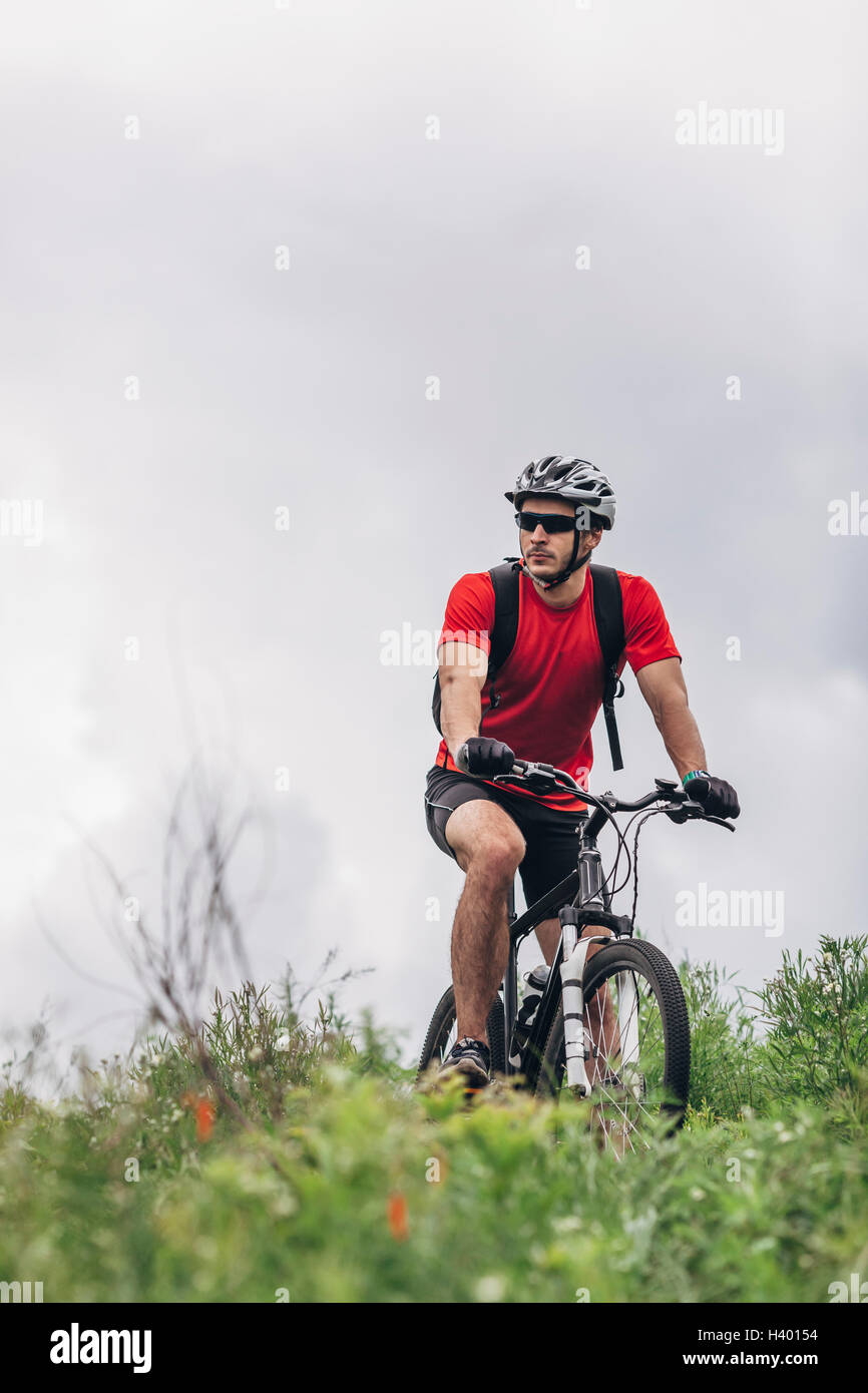 Zuversichtlich Mann Reiten Mountainbike gegen bewölktem Himmel Stockfoto