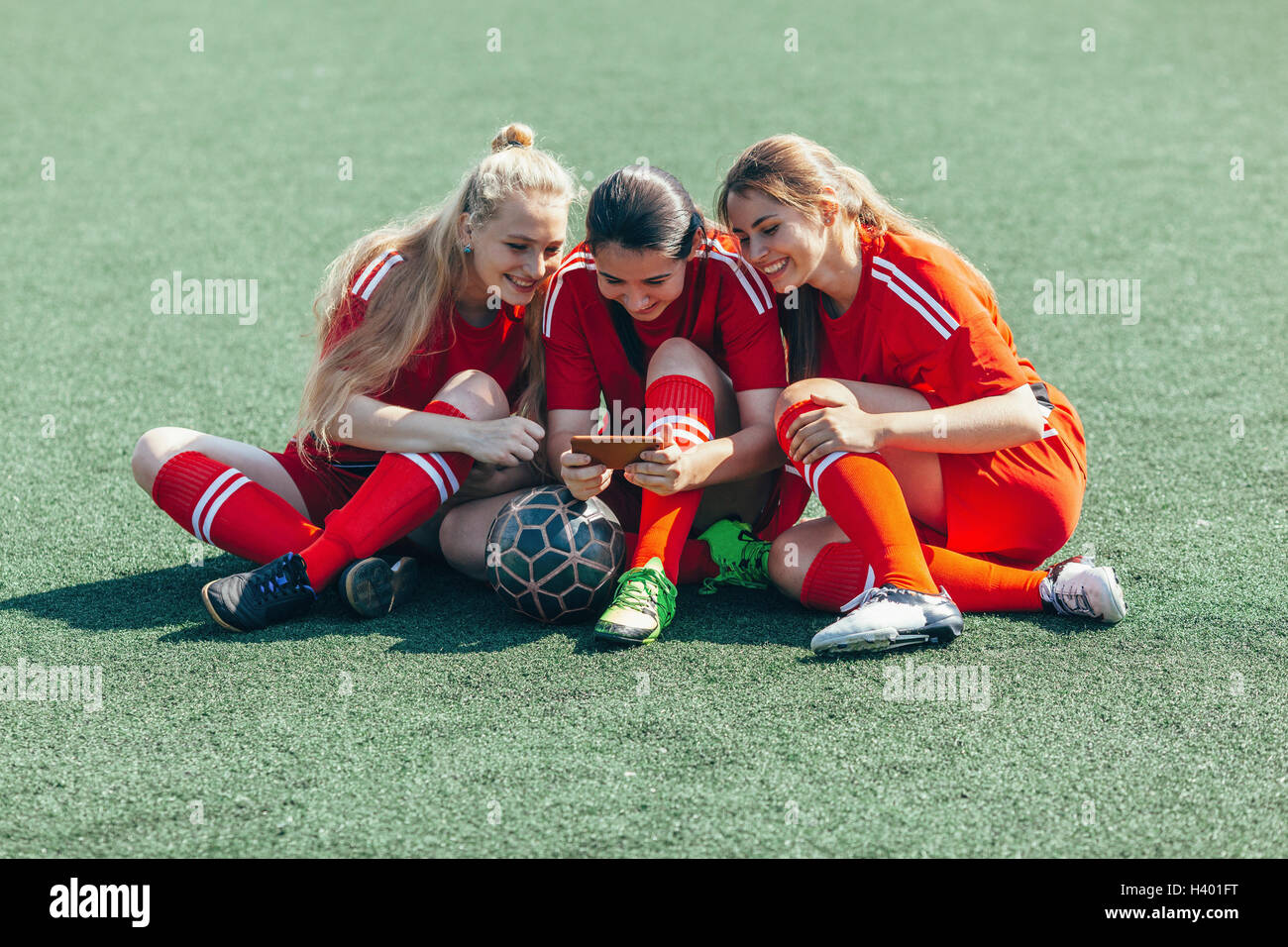 Fröhlich Fußball-Spieler mit Smartphone sitzend auf Feld Stockfoto