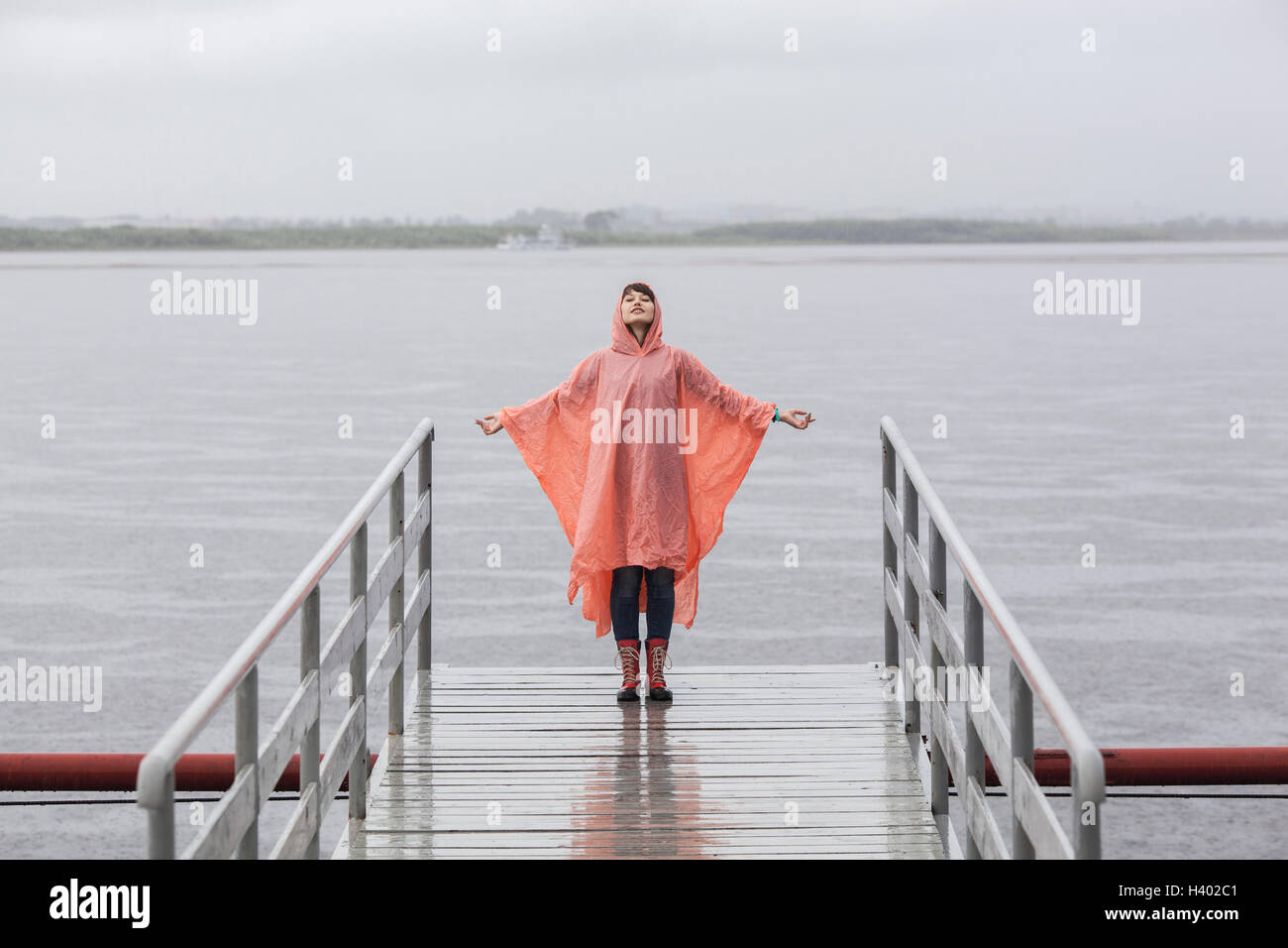 Frau trägt Regenmantel genießen Regenzeit auf Steg stehend Stockfoto