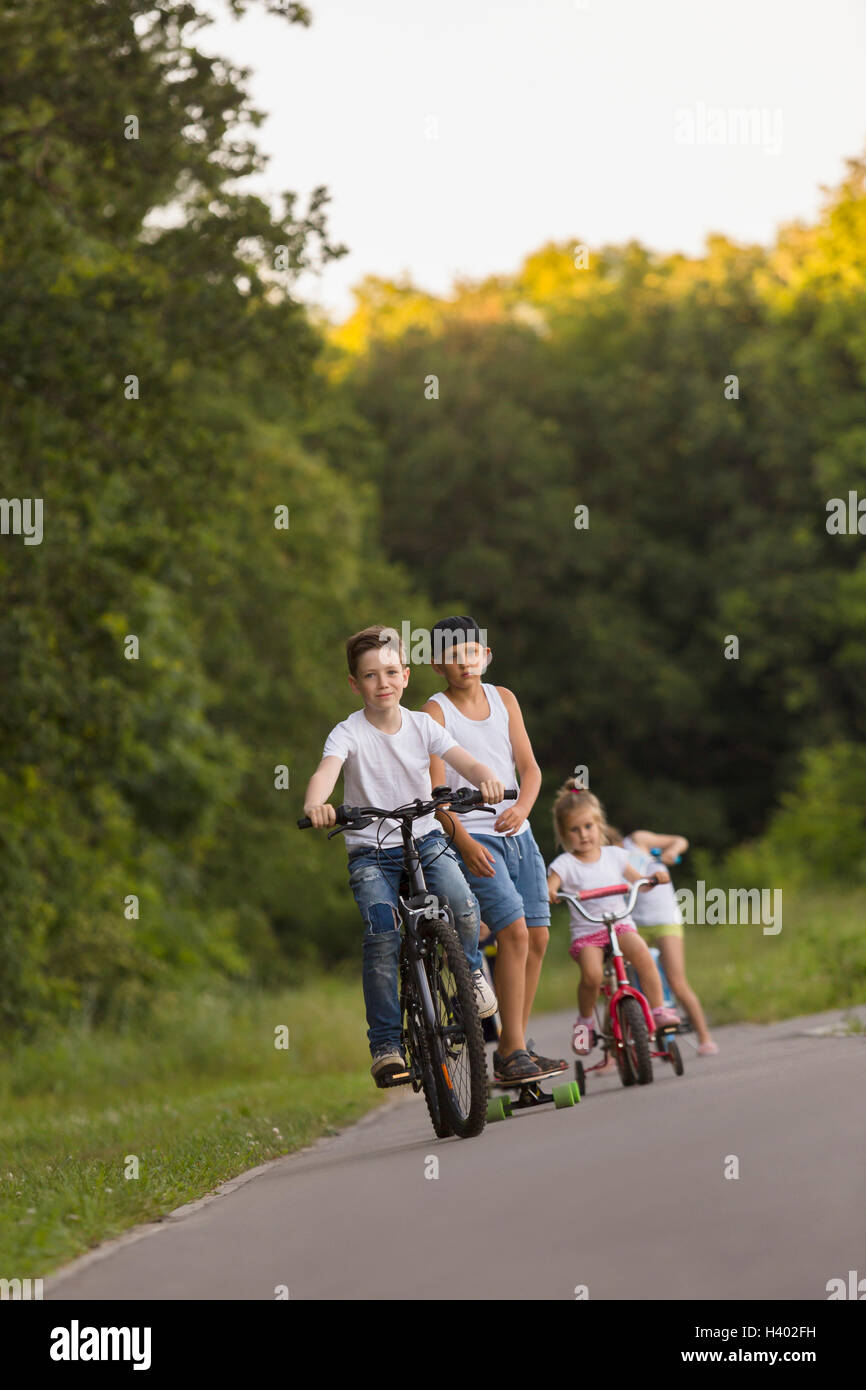 Geschwister, Radfahren auf der Straße gegen Bäume im park Stockfoto