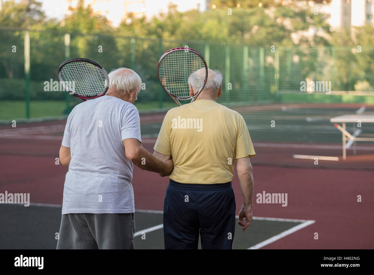 Rückansicht des Senioren Freunde tragen Tennisschläger bei einem Spaziergang am Spielfeld Stockfoto