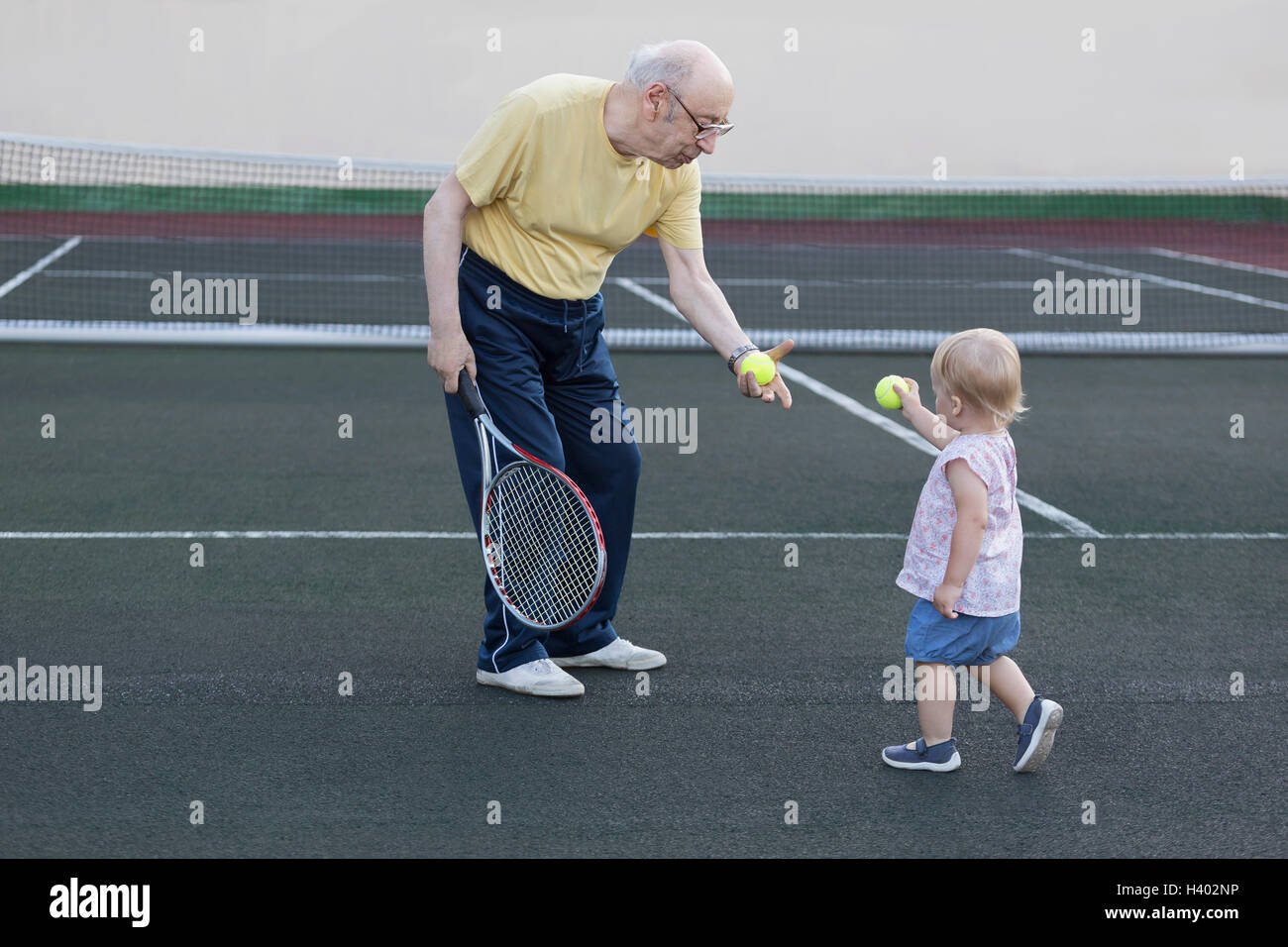 Mädchen, Tennisball, Großvater im stehen am Spielfeld Stockfoto