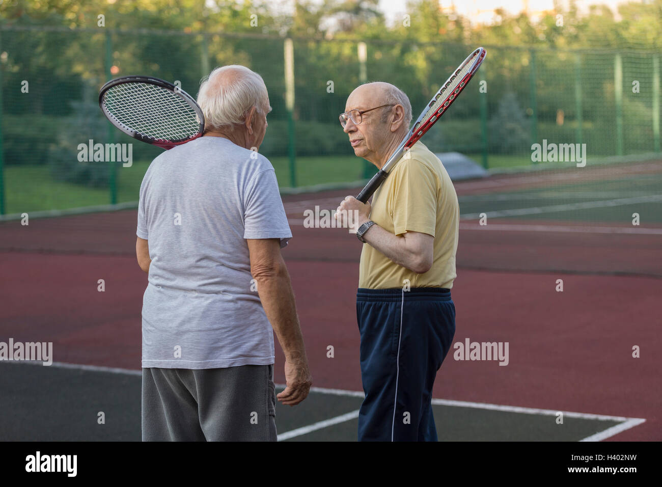 Senioren Freunde tragen Tennisschläger während des Gesprächs am Spielfeld Stockfoto