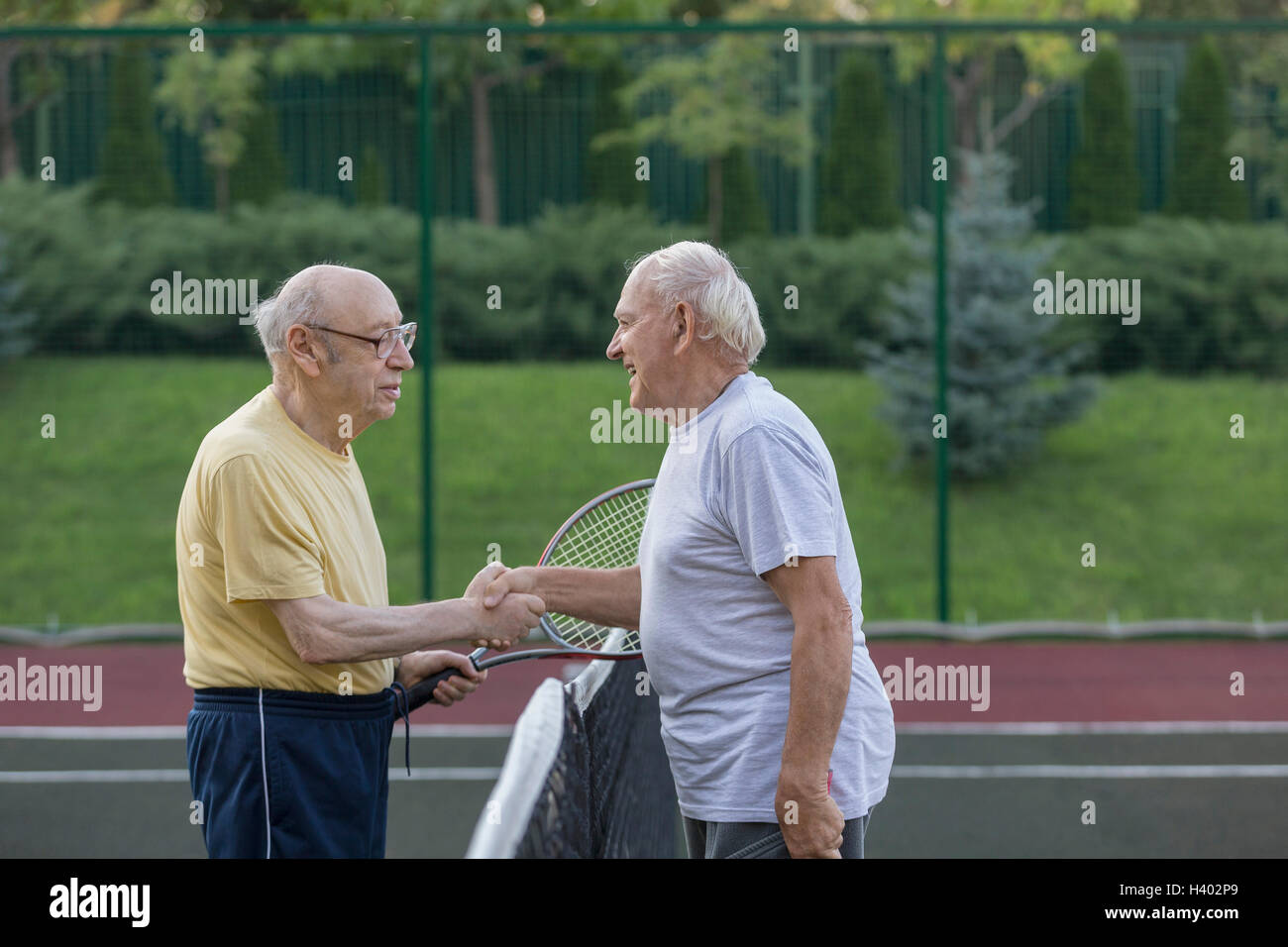 Senioren Freunde Händeschütteln über Netz auf Tennisplatz Stockfoto