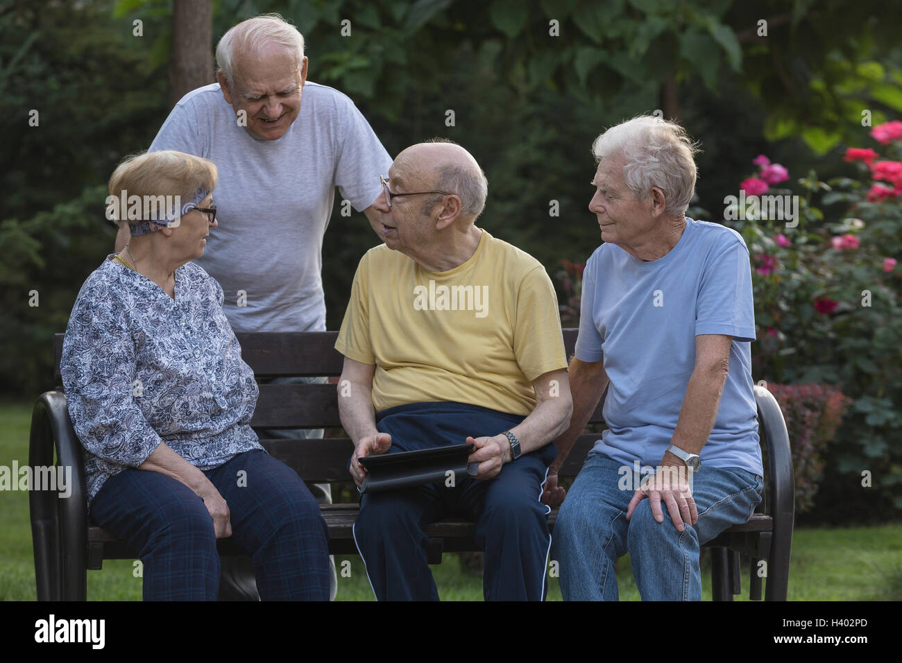 Lächelnden Senioren Freunde sprechen bei der Verwendung von digital-Tablette auf Parkbank Stockfoto