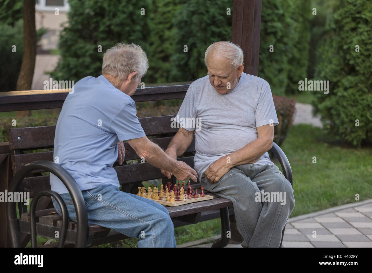 Senioren Freunde spielt Schach beim Sitzen auf der Parkbank gegen Bäume Stockfoto