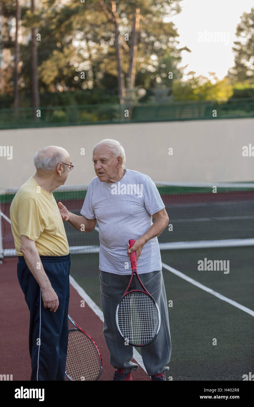 Senioren Freunde reden haltend Tennisschläger am Hof Stockfoto