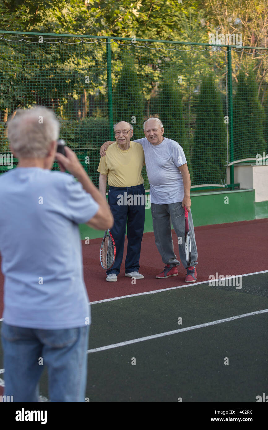 Rückansicht des Menschen fotografieren Freunde gegen Zaun am Tennisplatz Stockfoto