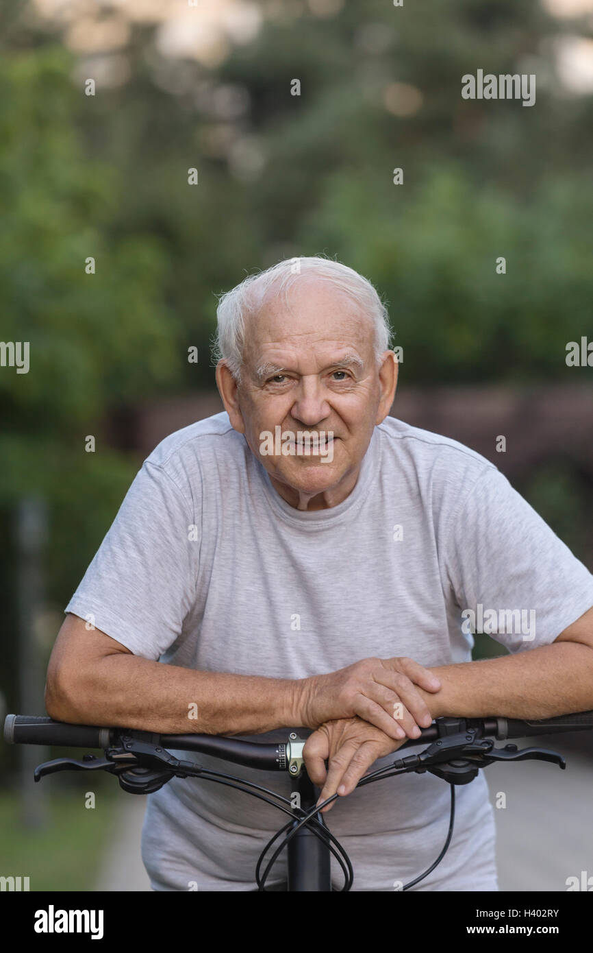 Portrait von senior Mann stützte sich auf dem Fahrrad im park Stockfoto