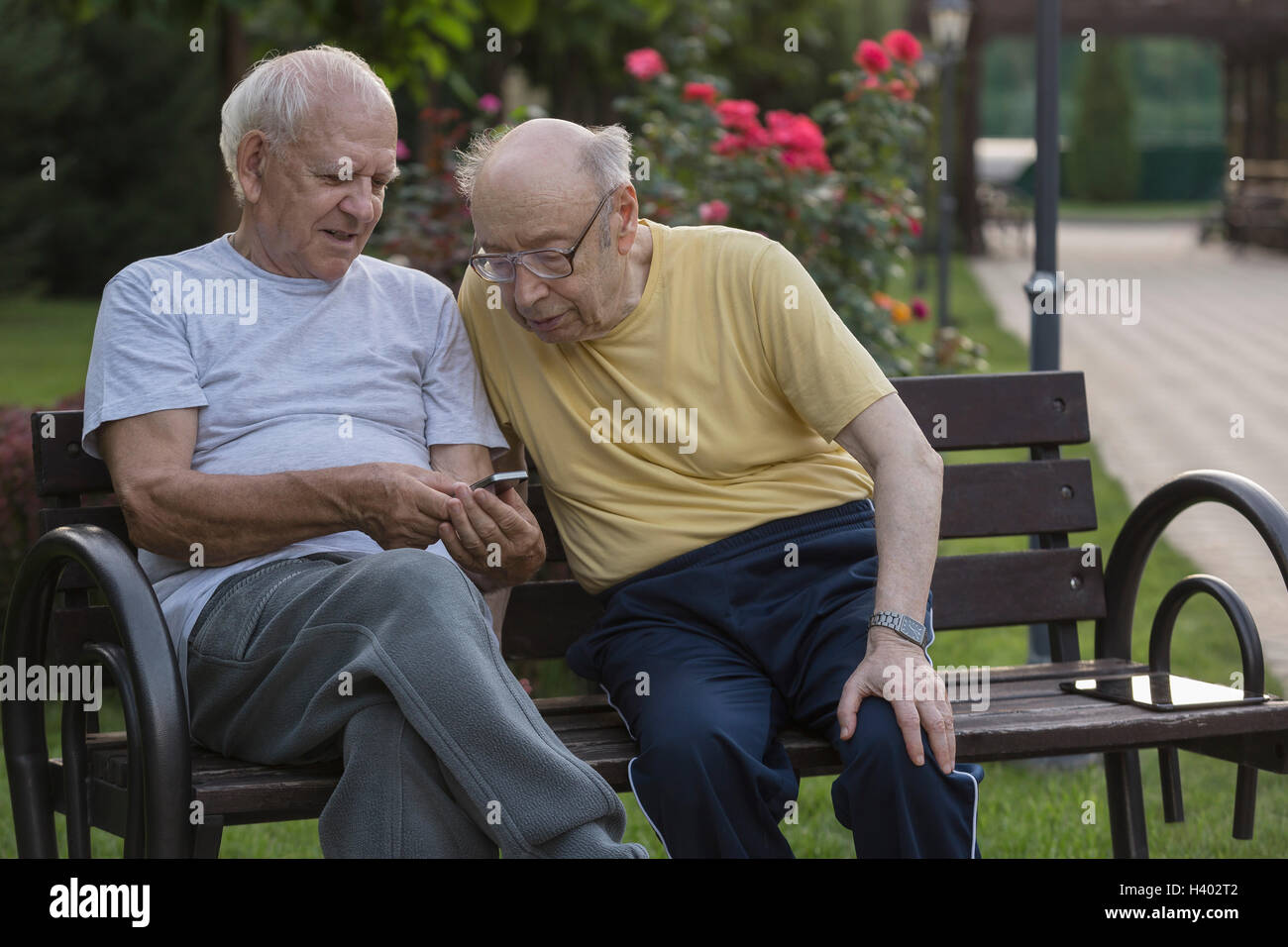 Senior woman zeigt Handy Freund beim Sitzen auf der Parkbank Stockfoto