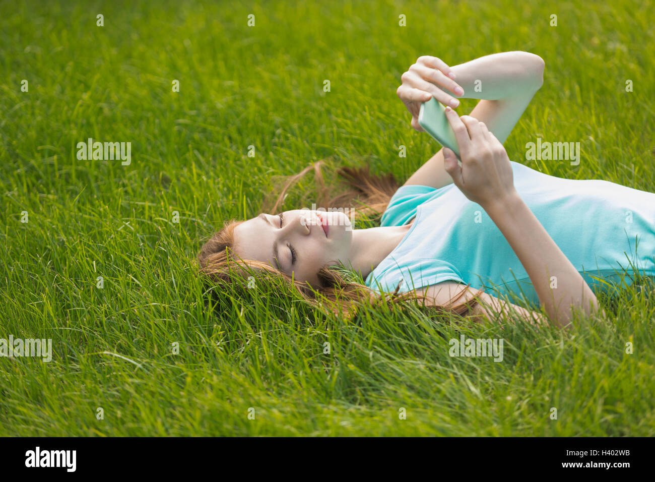 Junge Frau mit Telefon auf der Wiese liegend Stockfoto
