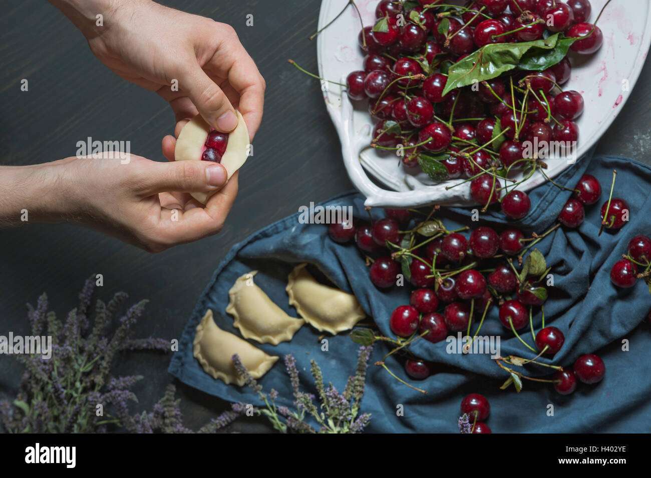 Bild von Händen Knödel mit Kirschen am Tisch füllen beschnitten Stockfoto