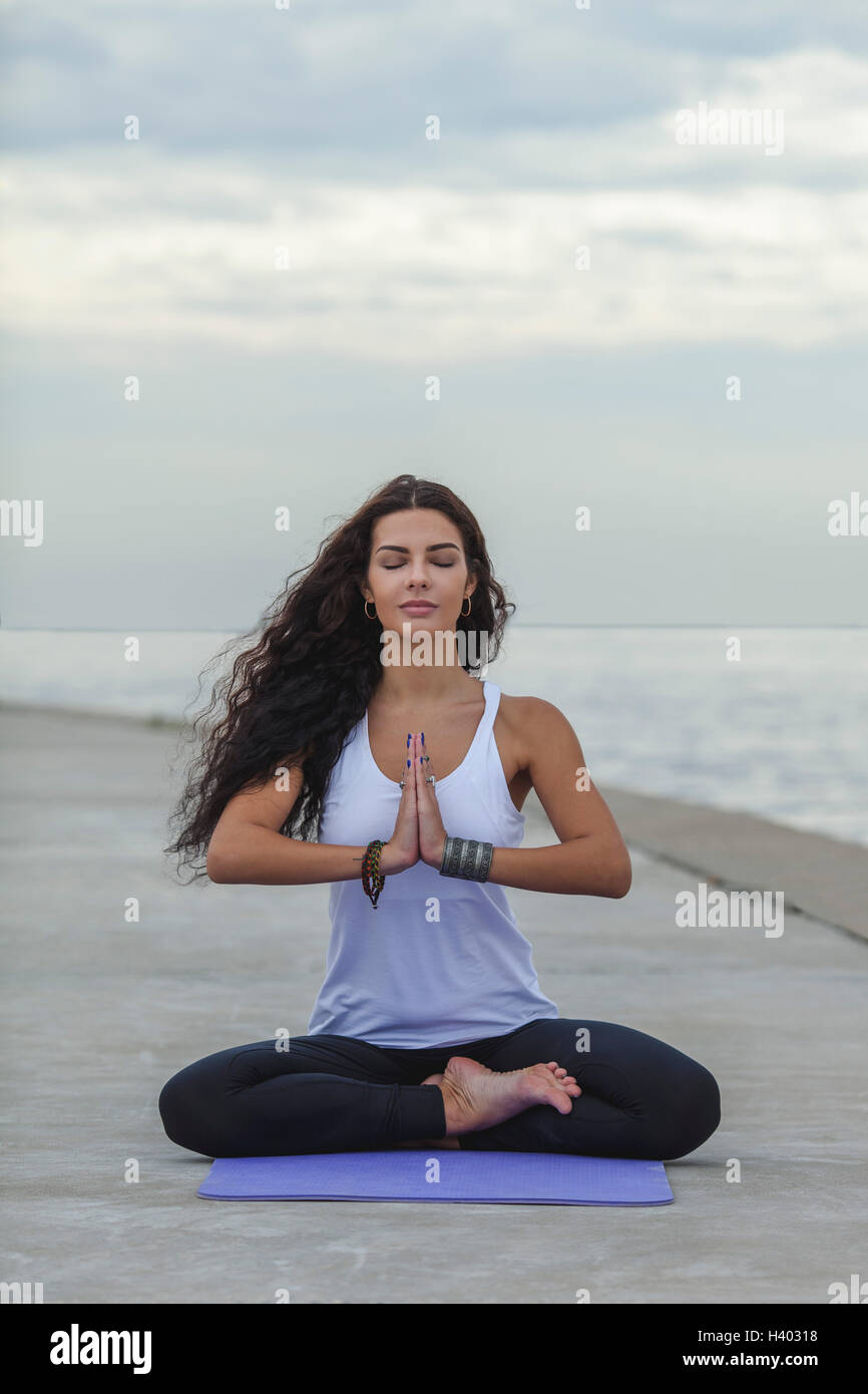 Frau mit geschlossenen Augen praktizieren Yoga im Gebet Position am Strand gegen bewölktem Himmel Stockfoto