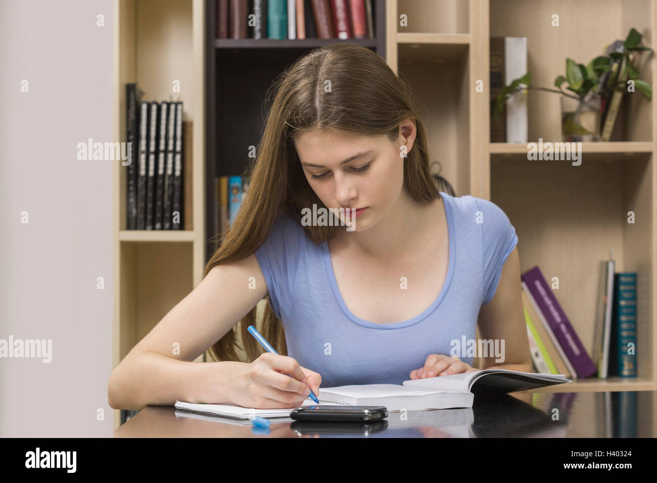 Ernsthaften Studenten beim Sitzen gegen Bücherregal Bibliothek Buch schreiben Stockfoto