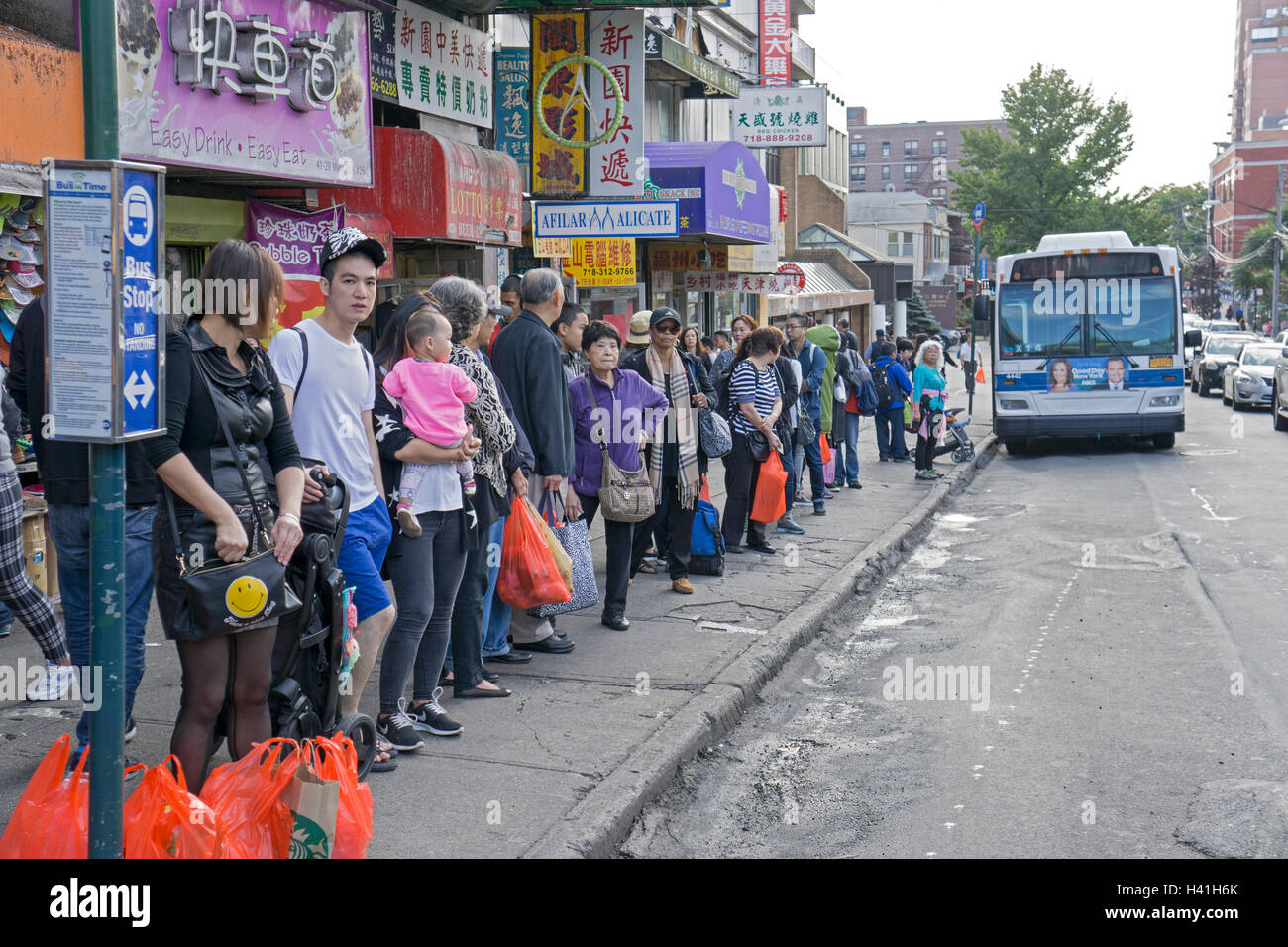 Ein gemischtes Publikum von Menschen warten auf ein City-Bus in der Innenstadt von Flushing, Queens, New York City. Stockfoto