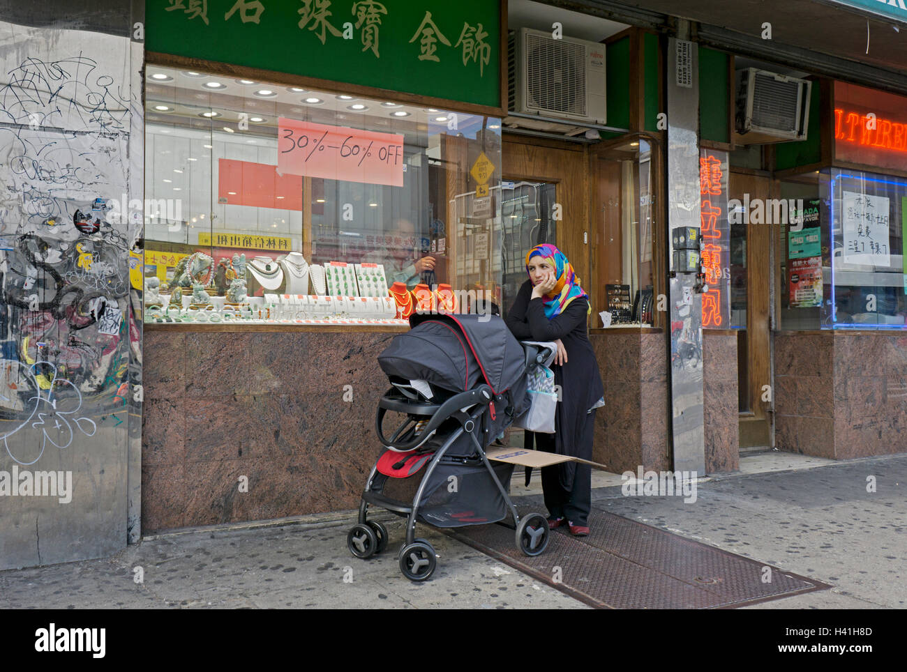 Eine muslimische Frau verlor in ihren Gedanken mit Kinderwagen vor einem Juweliergeschäft in der Roosevelt Avenue in Downtown Flushing, Queens. Stockfoto