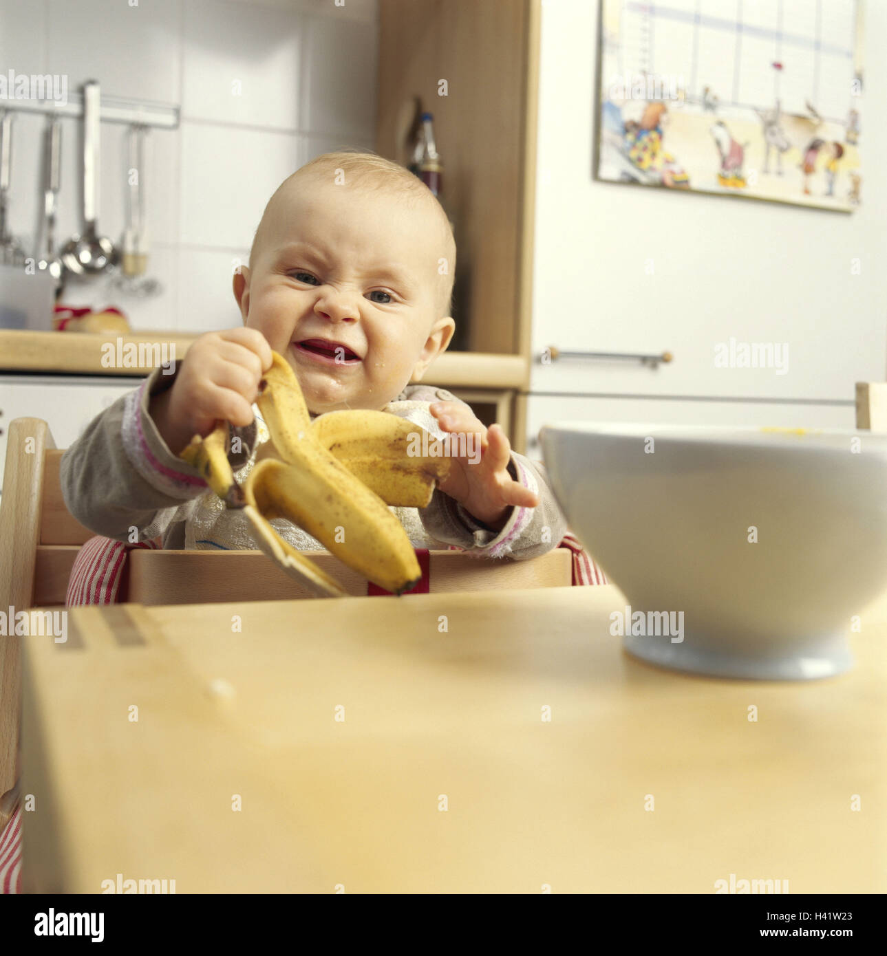 Baby, Kinderstuhl, Banane isst Kind 0-6 Monate, Kleinkind, sitzt, Lächtzchen, Drools, Schüssel, Hunger, Obst, Essen, Ernährung, Küche, Küchentisch, Gesundheit, Temperament, hilflos, energisch, Entwicklung, Unabhängigkeit Stockfoto