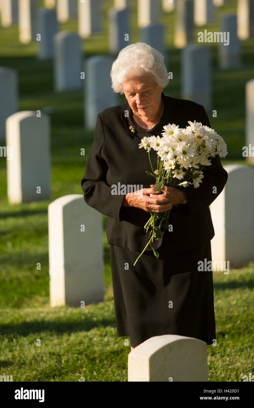 Kaukasische Witwe hält Strauß am Friedhof Grabstein Stockfoto