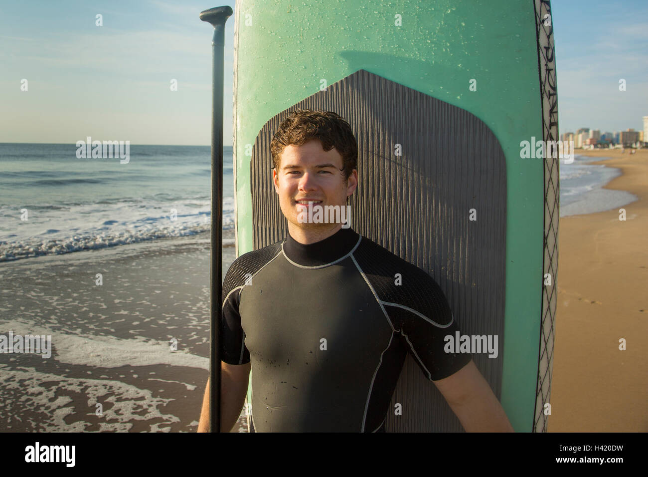 Mann posiert mit Paddleboard am Strand Stockfoto