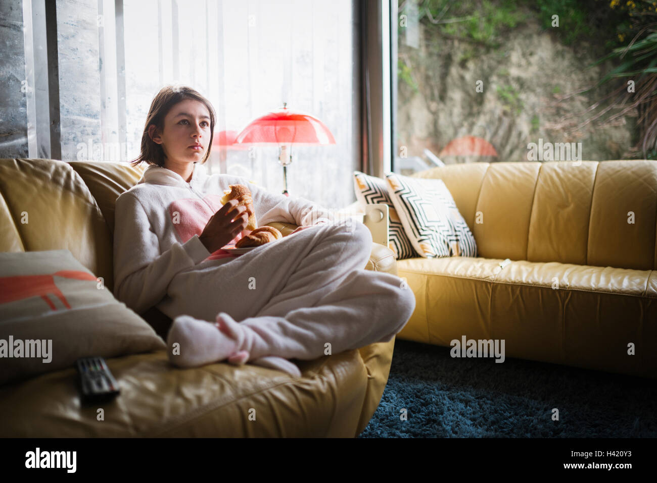 Gemischte Rennen Mädchen Hase Kostüm auf Sofa Croissant Essen Stockfoto