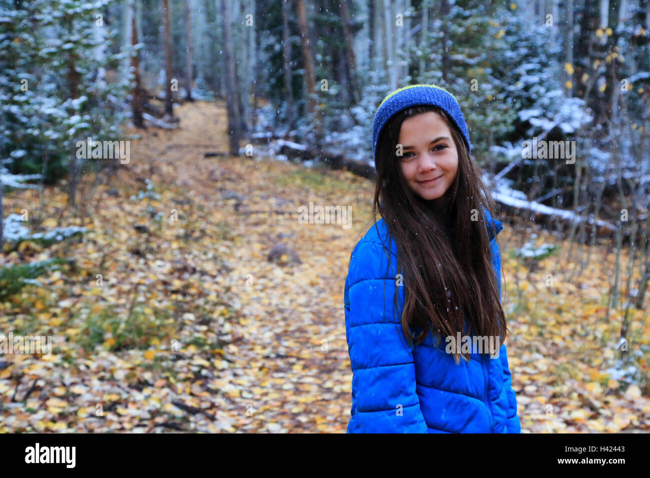 Eine Brünette Tween Mädchen tragen Winterkleidung Wanderungen im Wald. Sie trägt einen blauen Hut und einen blauen Mantel und lächelt. Stockfoto