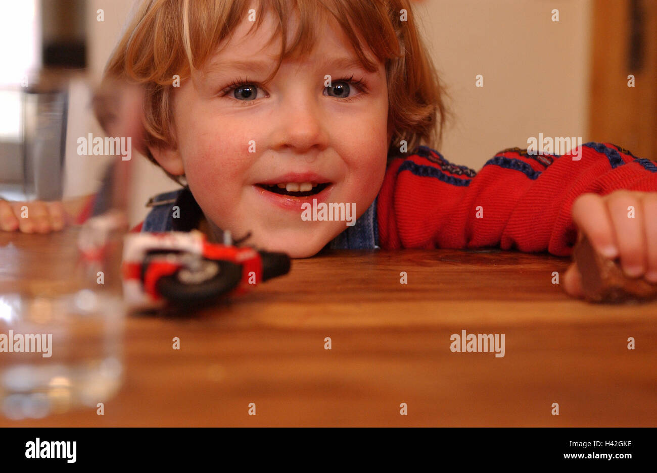 Junge, Ansicht Tischkante, Spielzeug, Porträt, Kind-Porträt, Kind, Kleinkind, 4-6 Jahre, glücklich, Kindheit, Lächeln, gute Laune, Spielzeug Motorrad, Wasserglas, gewellt Stockfoto