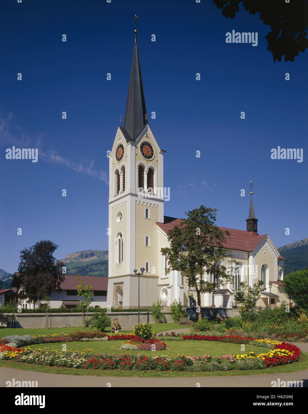 Österreich, Vorarlberg, Kleinwalsertal, Riezlern, Kirche Maria Opfer, Europa, Westösterreich, kleine Walsertal, Ort, Platz, Urlaubsort, Pfarrkirche, Kirche, Heilige Bau, Struktur, Architektur, Neubau, baut 1890 - 1892, Architekt Johann Mayer, Kirchturm, Garten, Blumen, Parkbank, Senior, sitzen, Sommer Stockfoto