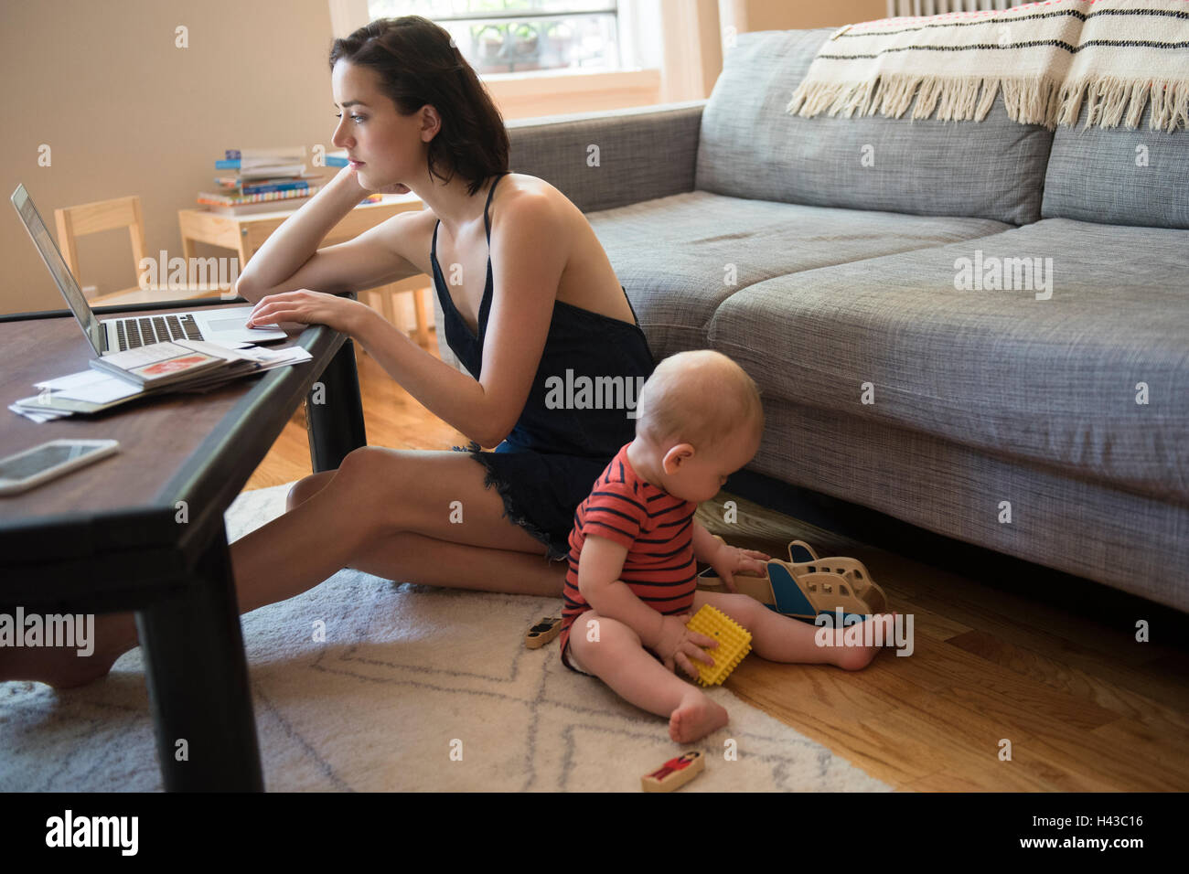 Kaukasische Mutter am Boden mit Laptop in der Nähe von Baby Sohn Stockfoto