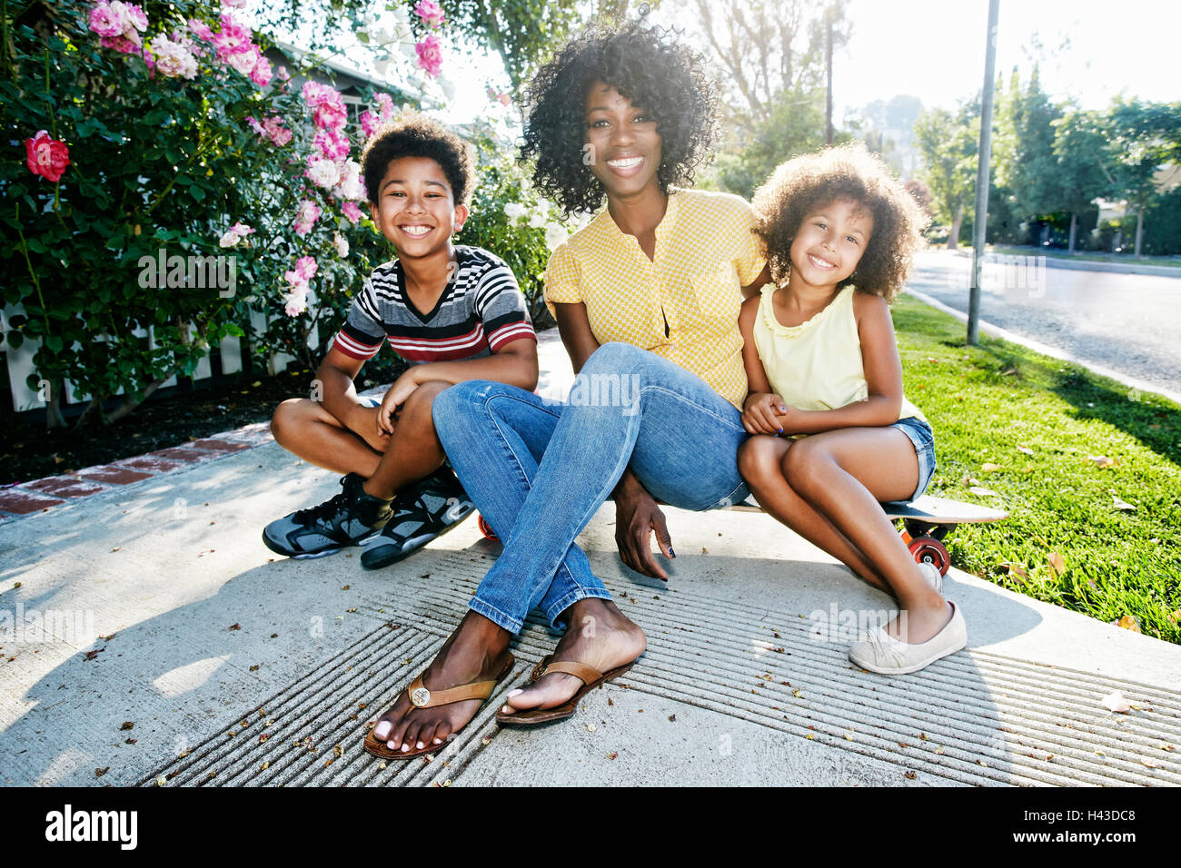 Lächelnde Mutter und Kinder sitzen auf Skateboard auf Bürgersteig Stockfoto