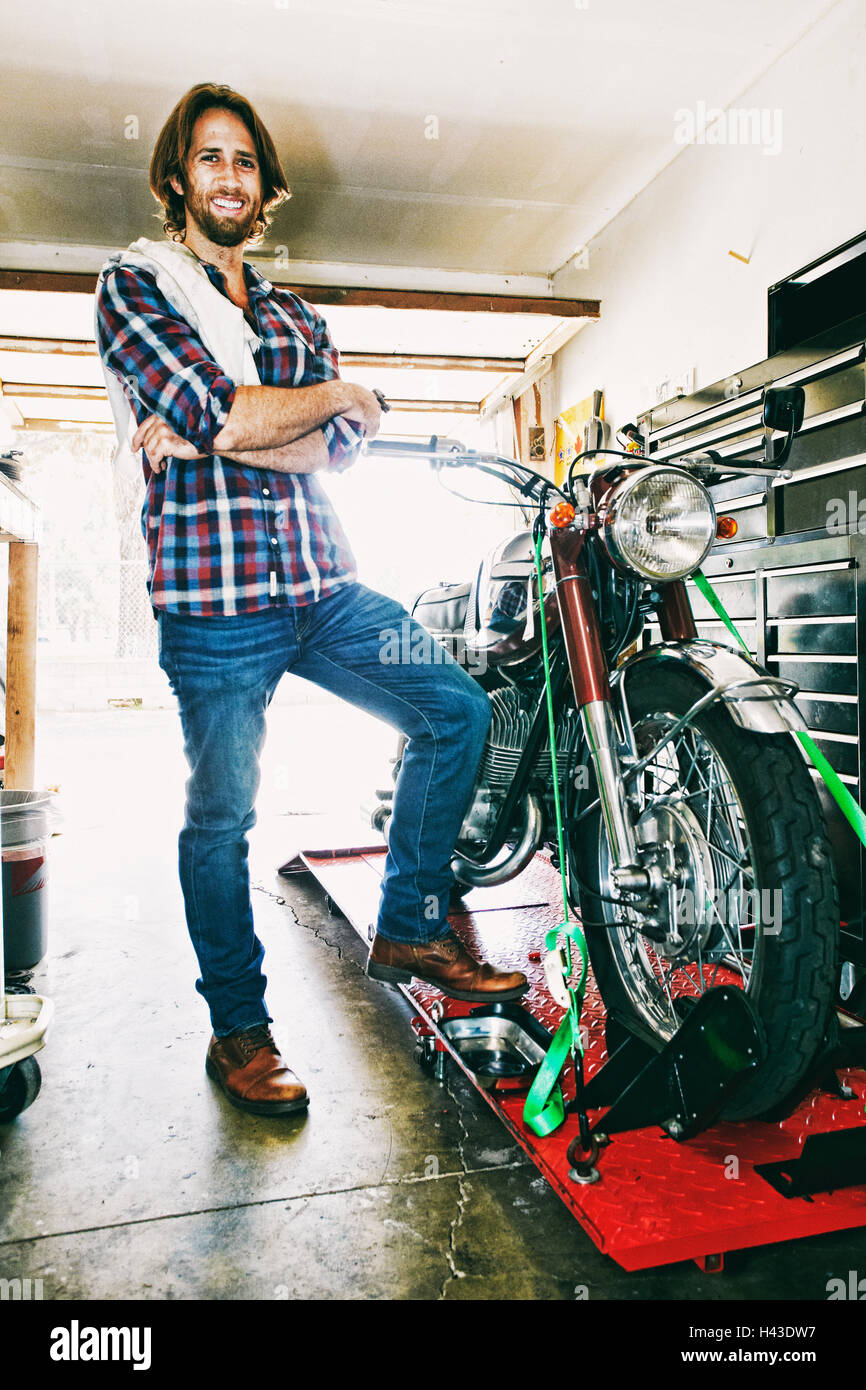 Kaukasischen Mann posiert mit Motorrad in garage Stockfoto