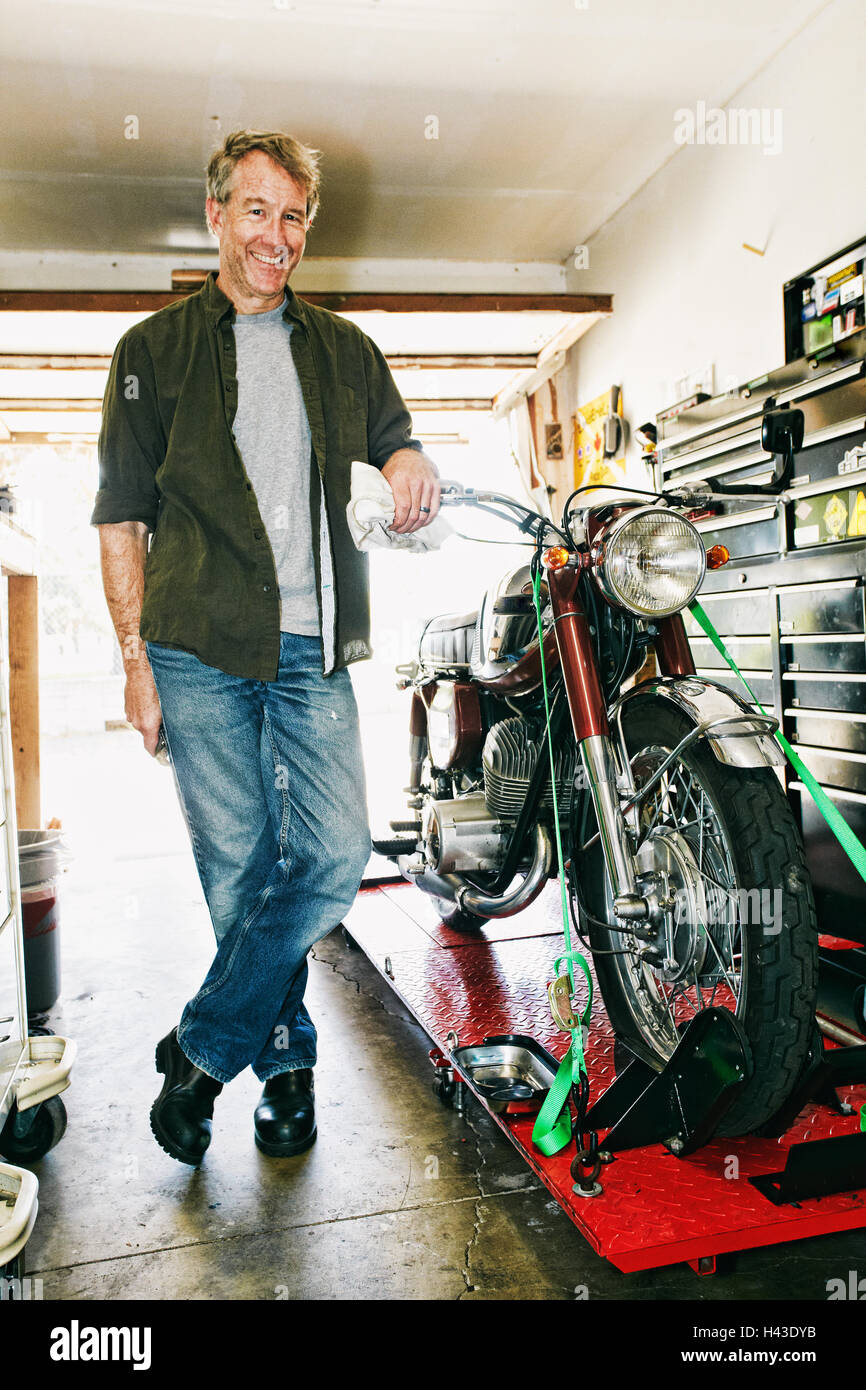 Kaukasischen Mann posiert mit Motorrad in garage Stockfoto