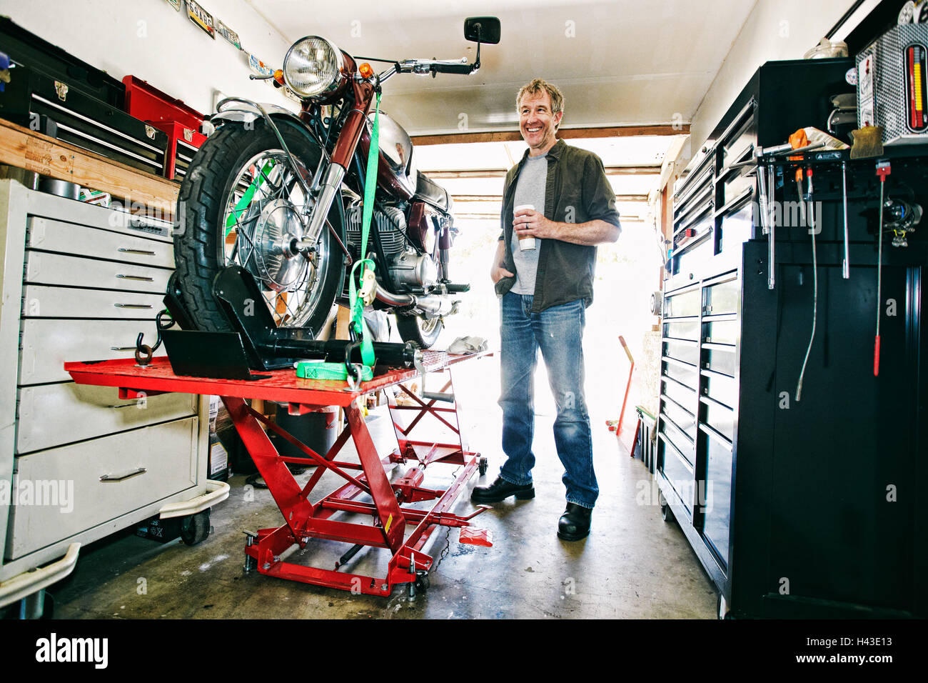 Kaukasischen Mann Kaffeetrinken während der Reparatur Motorrad in garage Stockfoto